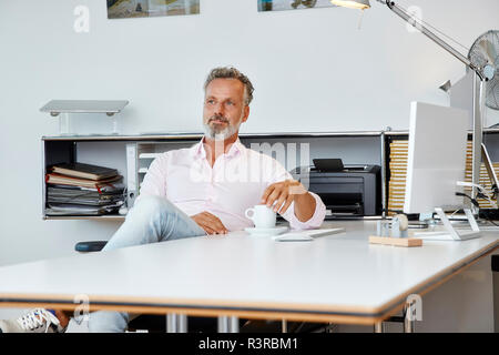 Businessman sitting at desk in office thinking Stock Photo