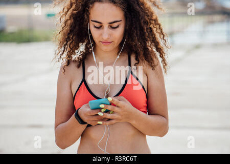 Young athletic woman wearing earbuds and using smartphone Stock Photo