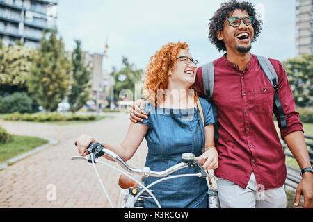Friends walking in park, talking, woman pushing bicycle Stock Photo