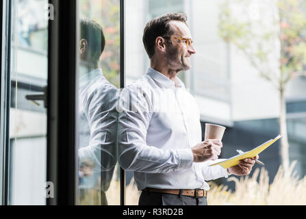 Laughing businessman with papers and coffee to go looking at distance Stock Photo