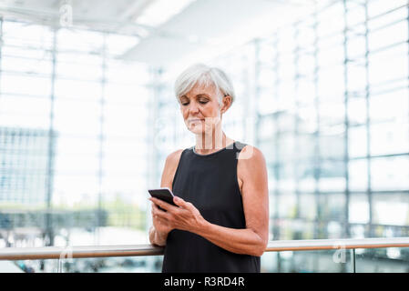 Senior woman standing at railing using cell phone Stock Photo