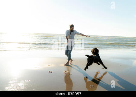 Young man running and playing with his dog on the beach Stock Photo