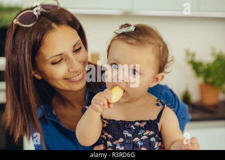Mother watching baby daughter eating an apple Stock Photo