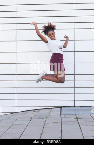 Portrait of laughing young woman jumping in the air Stock Photo