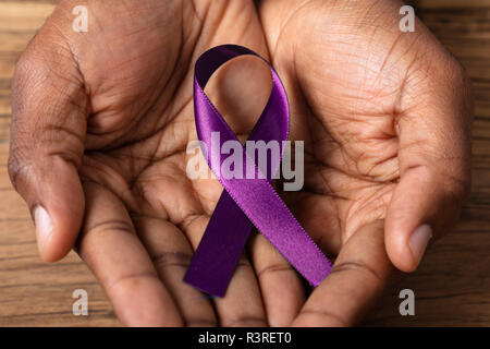 Close-up Of A Person's Hand Holding Ribbon To Support Alzheimer's Disease Awareness Stock Photo