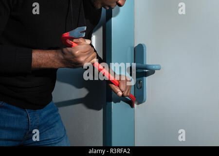 Thief In Black Hooded Sweatshirt Trying To Break The Door With Crowbar Stock Photo