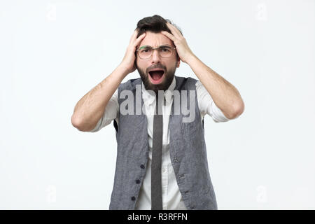 Excited crazy hispanic man yelling, touching head and screaming in panic as has many problems Stock Photo
