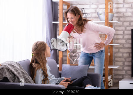 Mother Shouting Through Megaphone At Careless Girl Sitting On Sofa Using Digital Tablet Stock Photo