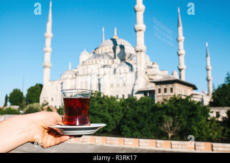 Woman holding cup of traditional Turkish tea on terrace with view of the Blue Mosque in Istanbul in Turkey.