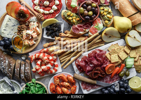 Italian antipasti snacks set. Brushettas, cheese variety, shrimps, salmon, olives, prosciutto with pear, salami and jamon over grey grunge table Stock Photo