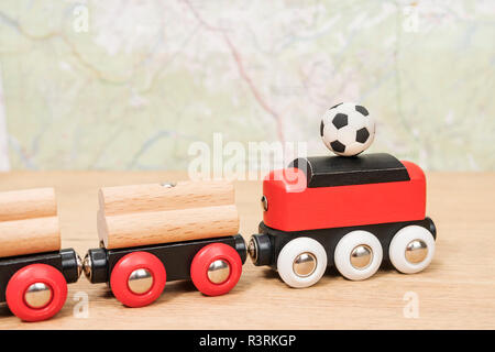 miniature soccer ball on the roof of a wooden toy train standing on the table against the background of the map Stock Photo