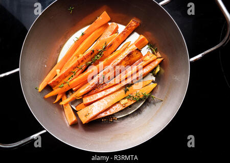 root vegetables, glazed carrots with thyme, ginger and honey in an iron pan on the black stove, high angle view from above Stock Photo