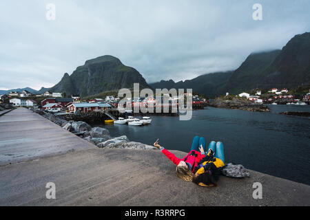 Norway, Lofoten, two young women lying on a pier at the coast taking a selfie Stock Photo