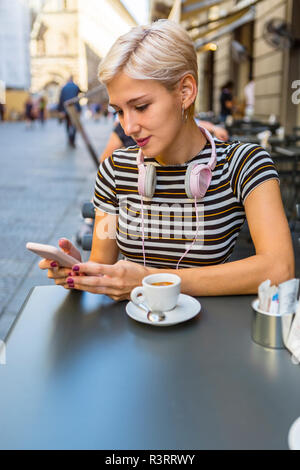 Italy, Florence, portrait of young woman at pavement cafe looking at smartphone Stock Photo