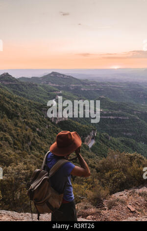 Spain, Barcelona, Montserrat, man with backpack taking photo of view at sunset Stock Photo