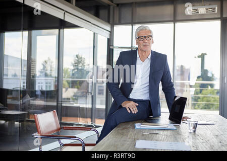 Successful manager sitting on desk, thinking Stock Photo