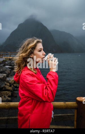 Norway, Lofoten, young woman at the coast drinking from takeaway coffee Stock Photo