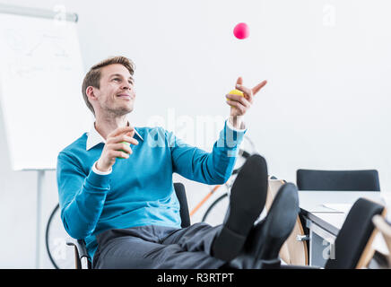 Smiling businessman juggling with balls in office Stock Photo