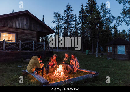 Group of friends sitting at a campfire, talking and drinking tea Stock Photo