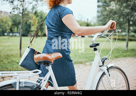 Young woman walking in park, pushing bicycle Stock Photo