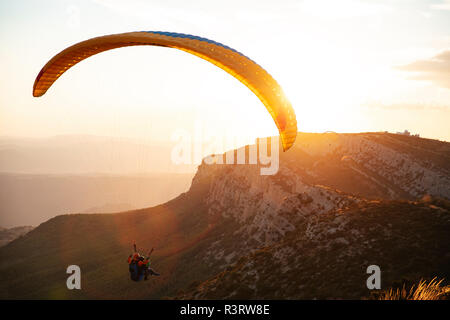 Spain, Silhouette of paraglider soaring high above the mountains at sunset Stock Photo