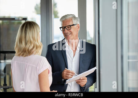 Businessman and woman standing in office, discussing project, holding documents Stock Photo