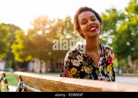Portrait of smiling young woman on bench in a park Stock Photo