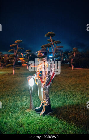 Spaceman standing at a lamp in a park at night Stock Photo