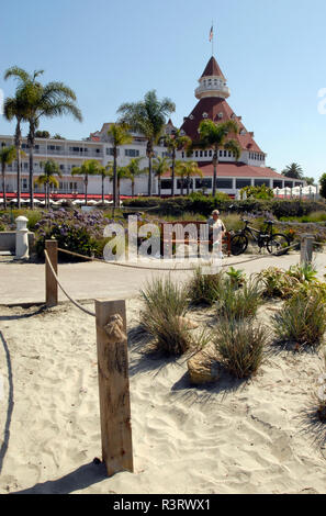 A cyclist rests along a path near the historic Hotel del Coronado near San Diego, California. The landmark Victorian beach resort opened in 1888. Stock Photo