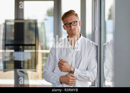 Portrait of grimacing businessman in office leaning against window Stock Photo