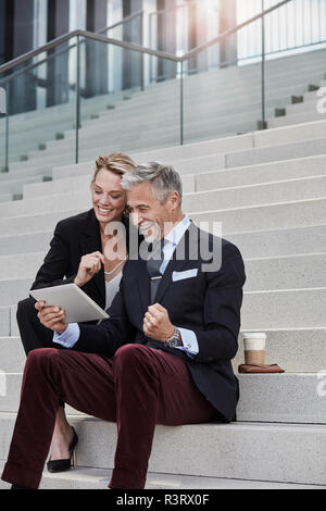 Two business people sitting together on stairs looking at tablet Stock Photo