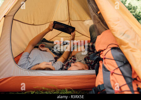 Young couple relaxing in tent, using digital tablet Stock Photo