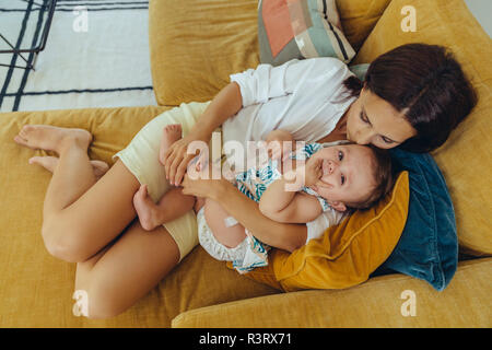 Mother cuddling and kissing her baby girl on couch Stock Photo