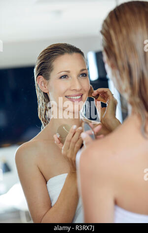 Mirror image of smiling blond woman applying makeup Stock Photo