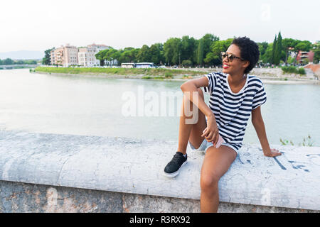 Smiling young woman wearing sunglasses sitting at the riverside Stock Photo