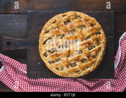 Baked whole round apple pie on a rectangular old brown board, wooden table, top view Stock Photo