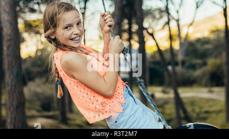 Happy girl swinging on a tyre swing in a park. Girl having fun standing on a tire swing in a park. Stock Photo