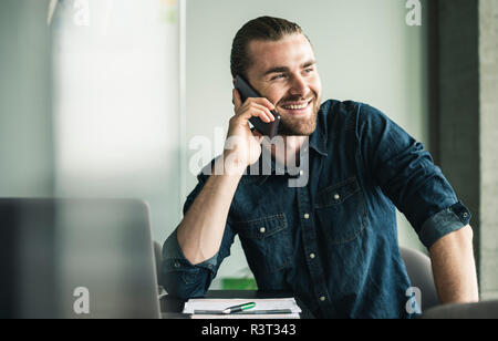 Smiling young businessman on cell phone in office Stock Photo