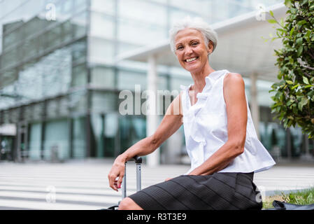 Portrait of happy senior woman with baggage sitting in the city Stock Photo