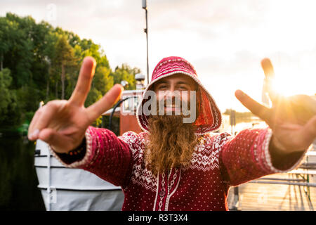 Finland, Kajaani, Cheerful young man. wearing houded jacket, standing on jetty, making hand gestures Stock Photo