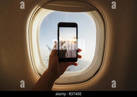 Hand taking cell phone picture out of plane window Stock Photo
