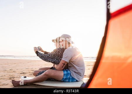 Couple camping on the beach, taking smartphone selfies Stock Photo