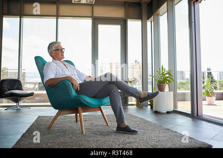 Mature man relaxing in armchair at the window at home Stock Photo