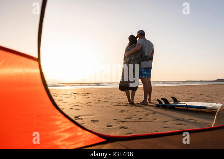 Romantic couple camping on the beach, embracing at sunset Stock Photo