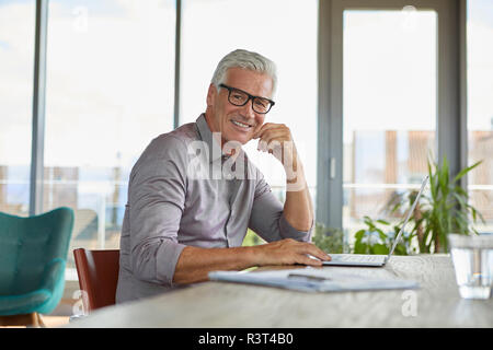 Portrait of smiling mature man using laptop on table at home Stock Photo