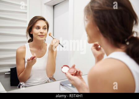 Mirror image of smiling young woman applying Makeup in bathroom Stock Photo