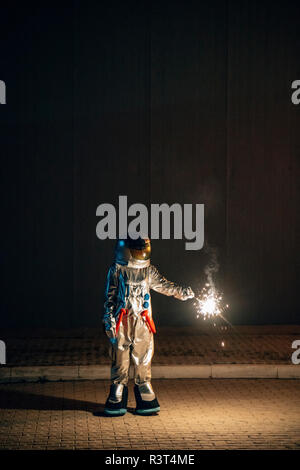 Spaceman standing on a road at night holding sparkler Stock Photo