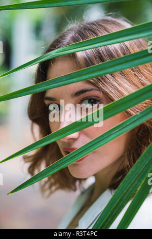 Young woman looking through palm leaf, portrait Stock Photo