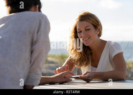 Young couple using digital tablet, sitting a ta a table at the beach Stock Photo