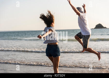 Young couple having fun on the beach, running and jumping at the sea Stock Photo